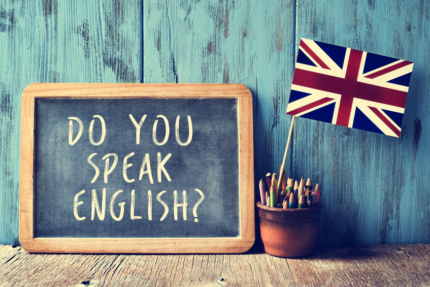 a chalkboard with the text do you speak english? written in it, a pot with pencils and the flag of the United Kingdom, on a wooden desk, with a filter effect