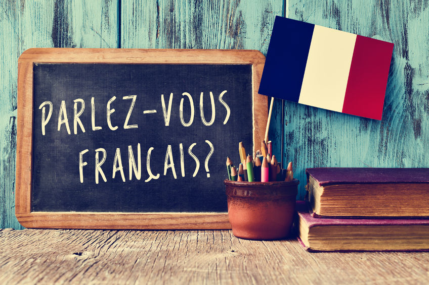 46480434 - a chalkboard with the question parlez-vous francais? do you speak french? written in french, a pot with pencils and the flag of france, on a wooden desk
